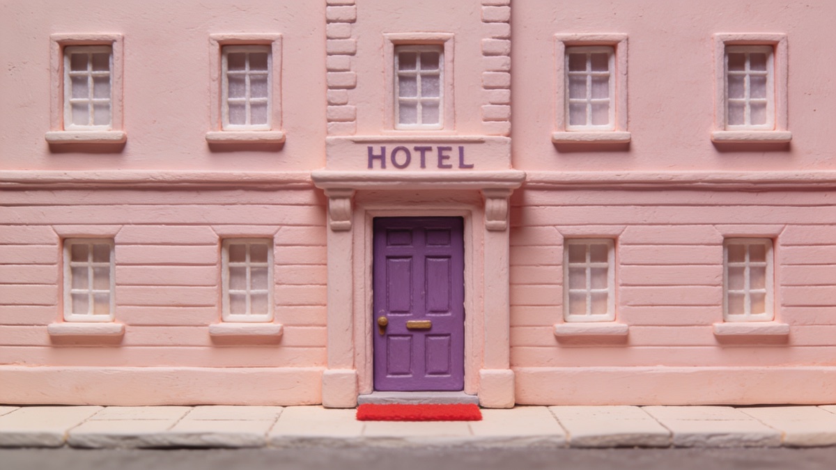 Hotel cor-de-rosa em miniatura, de frente e simétrico, com uma escadaria central e janelas alinhadas