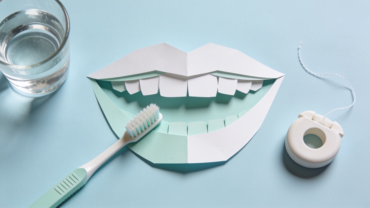 Escova de dentes, fio dental e um copo de água sobre uma bancada clara de banheiro